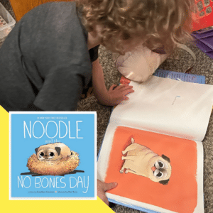 a toddler looking at the book Noodle and the No Bones Day, a childrens book about Noodle the Pug